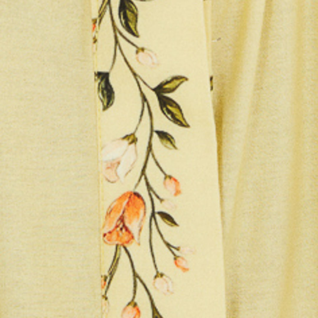 Detalle del estampado del vestido con elementos botánicos y frutas sobre un fondo amarillo claro.