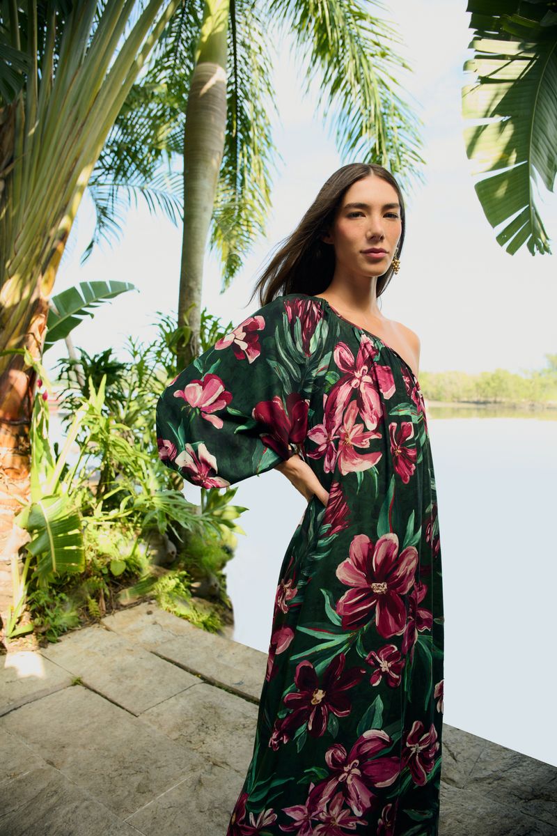 Primer plano de una mujer vistiendo un vestido largo con estampado floral, destacando el diseño de un solo hombro y el patrón vibrante.