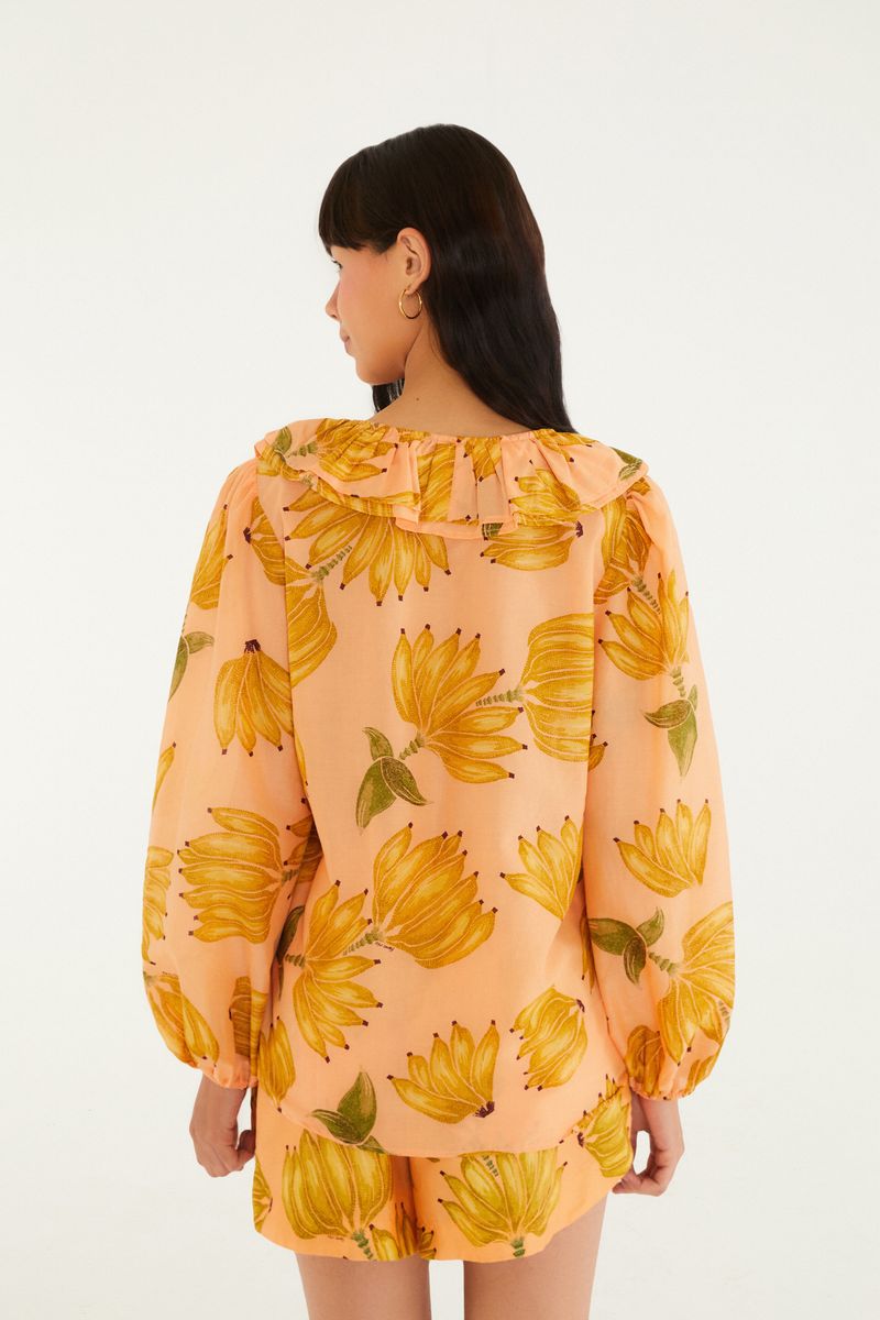 Vista trasera de una blusa estampada con tema botánico, destacando bananas en tonos vibrantes sobre fondo rosado claro.