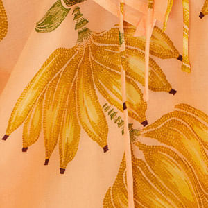 Detalle del estampado botánico con bananas en tonos vibrantes sobre fondo rosado claro.