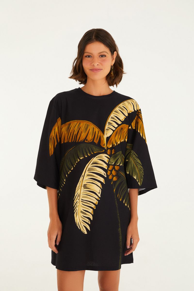 Vestido tipo camiseta con estampado de palmeras en tonos verdes y naranjas sobre fondo negro, visto desde el frente.