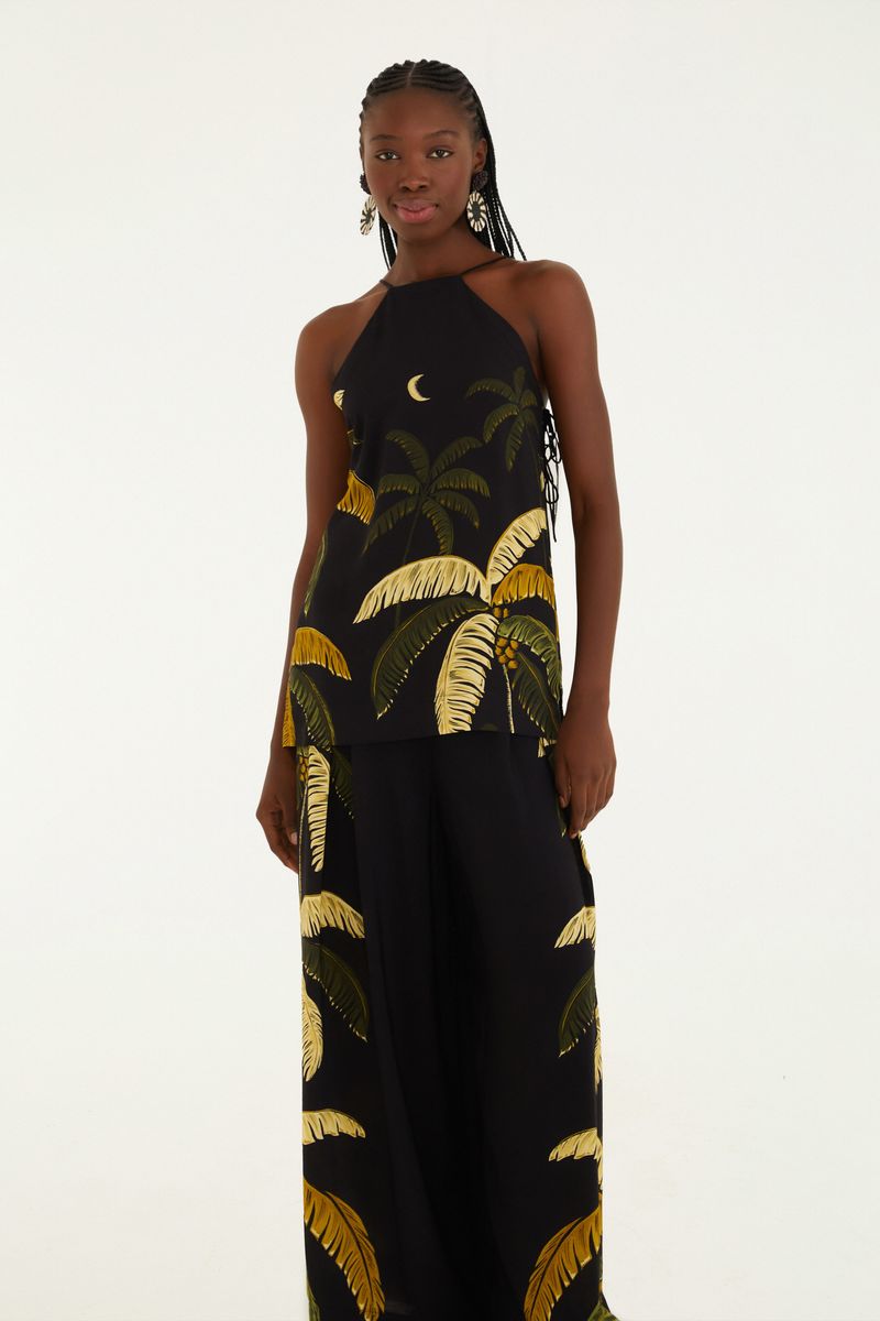 Modelo vistiendo pantalón negro con estampado tropical de follaje amarillo, combinado con top estampado.