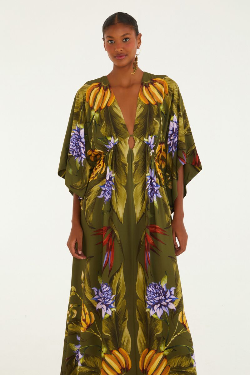 Vestido largo con estampado tropical sobre fondo verde, escote profundo y mangas amplias.