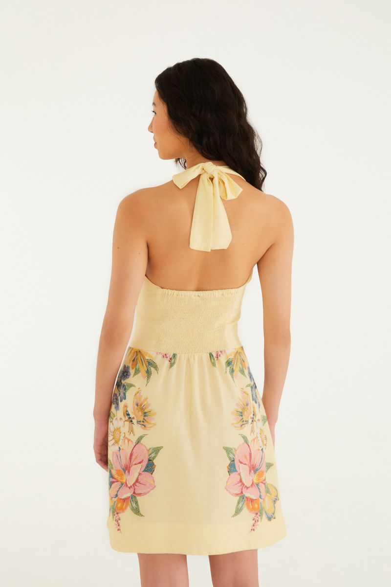 Vista trasera del vestido corto con estampado floral sobre fondo amarillo, mostrando el detalle de las tiras.