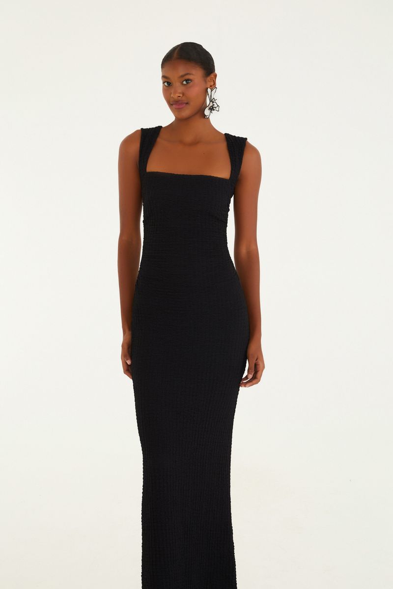 Vestido midi negro con tirantes torcidos visto de espaldas, mostrando el diseño elegante y la caída.