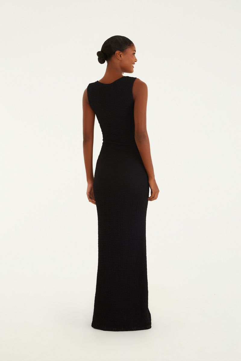 Vestido midi negro con tirantes torcidos visto de perfil, destacando la silueta y el largo.