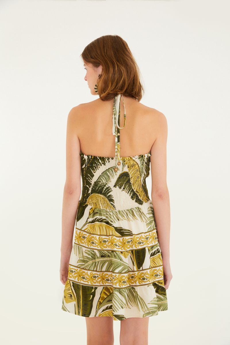 Detalle del estampado tropical del vestido corto, con elementos botánicos y ornamentos en tonos verdes y amarillos.