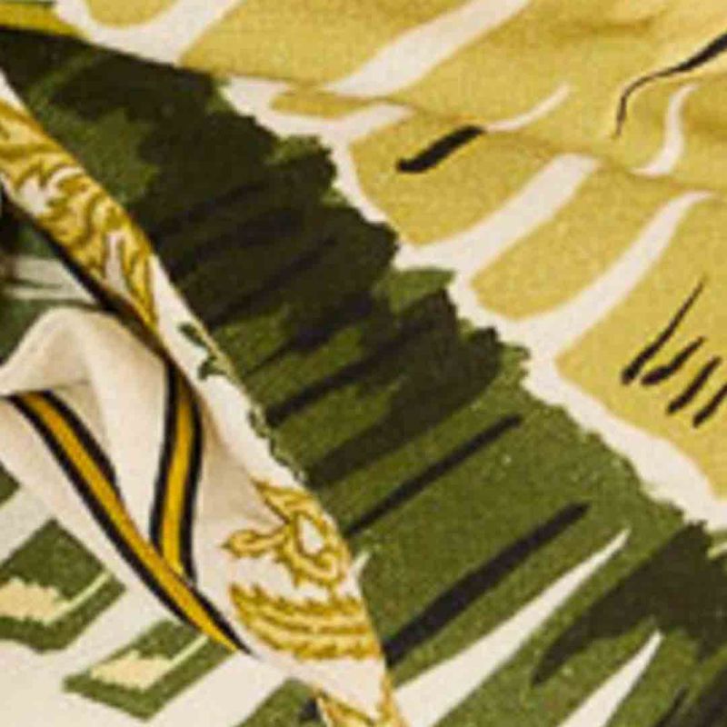 Detalle del estampado del vestido mostrando hojas y ornamentos en tonos de verde y amarillo.