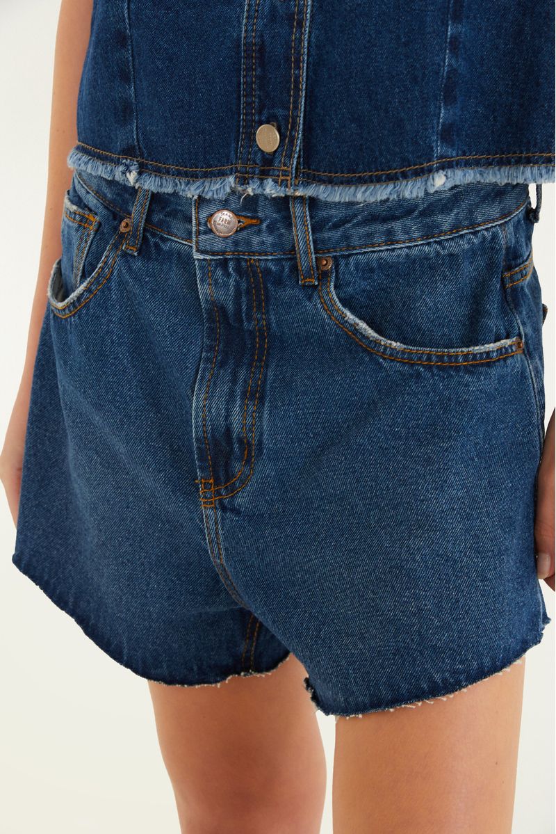 Close-up del cinturón del short jeans, mostrando el botón y los bolsillos frontales.