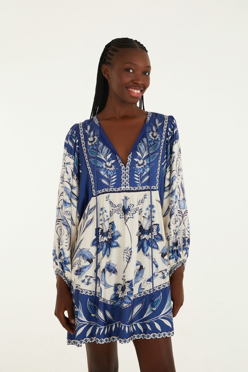 Vestido corto estampado con detalles florales en azul y blanco, escote en V y mangas largas.