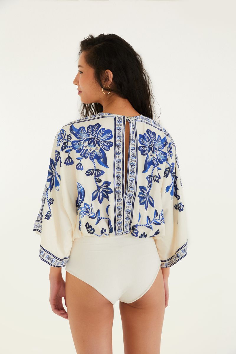 Body con estampado tropical azul y fondo beige, visto desde atrás.