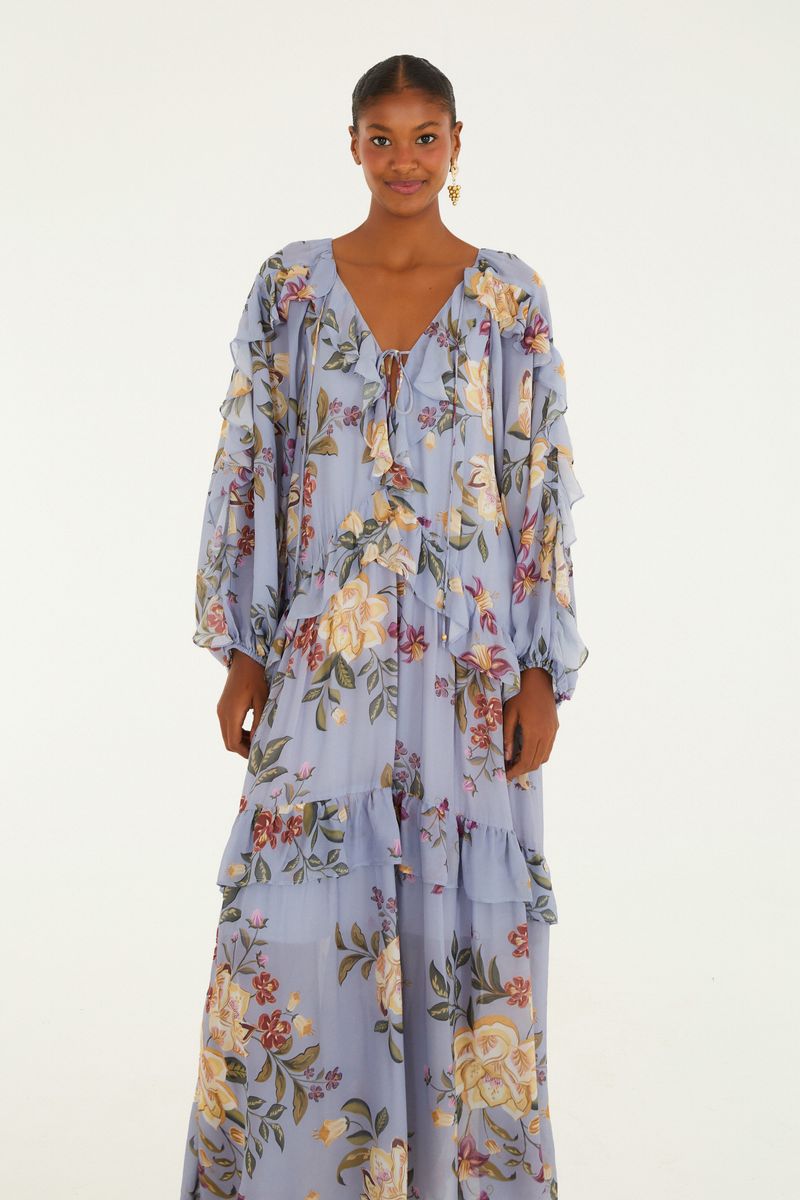 Vestido largo floral con volantes en fondo azul claro, mostrado de lado.