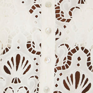 Close-up del tejido laise y de la fila de botones perlados, destacando textura y recortes