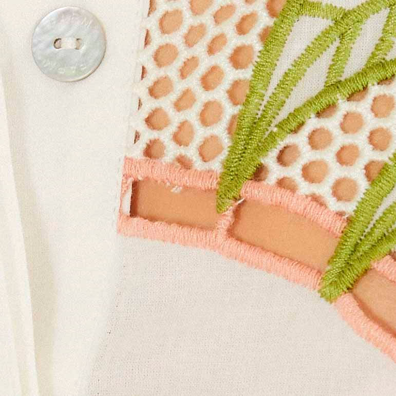 Vista trasera de la camisa exhibiendo motivos en V en tonos coral y verde y borde con bordado circular destacado, mostrando el ajuste suelto
