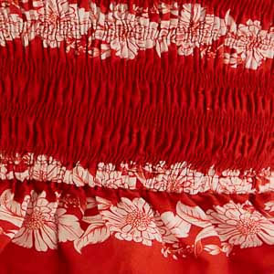 Primer plano de la textura fruncida y el estampado floral blanco sobre rojo en el top Farm, mostrando el elástico fruncido y acabado con volantes.