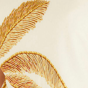 Vista trasera del vestido de un solo hombro Paisaje Tropical en viscosa beige, destacando el bordado de palmeras a lo largo de la espalda y el dobladillo con detalle dorado.